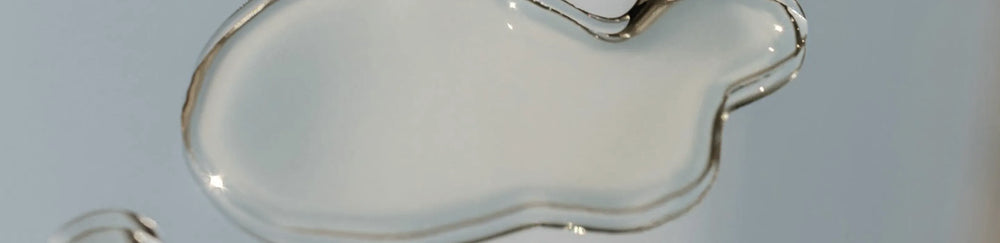 Clear viscous skincare serum droplet with a glossy texture on a light blue background